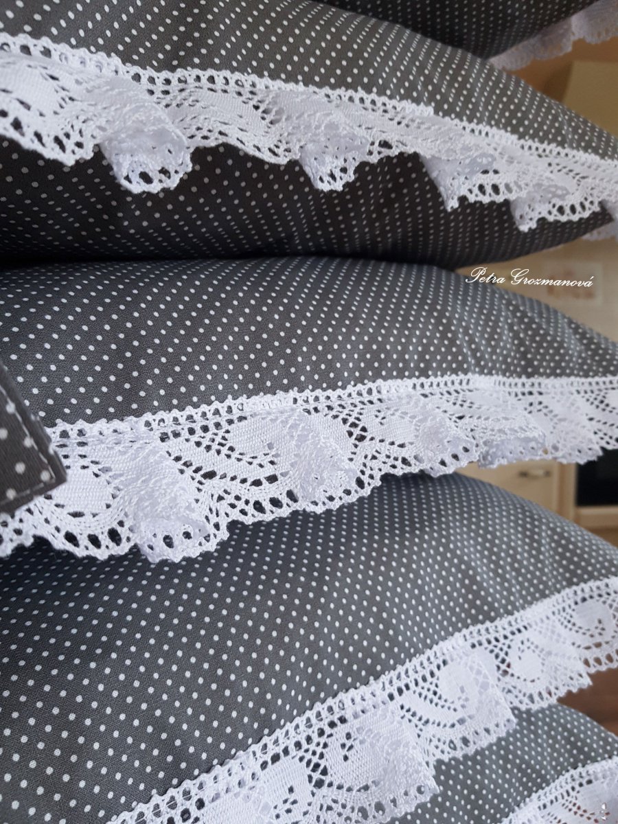 Sedák v šedém provedení s motivem bílých puntíků, lemovaný krajkou šíře 45 mm včetně výplně s úvazy.